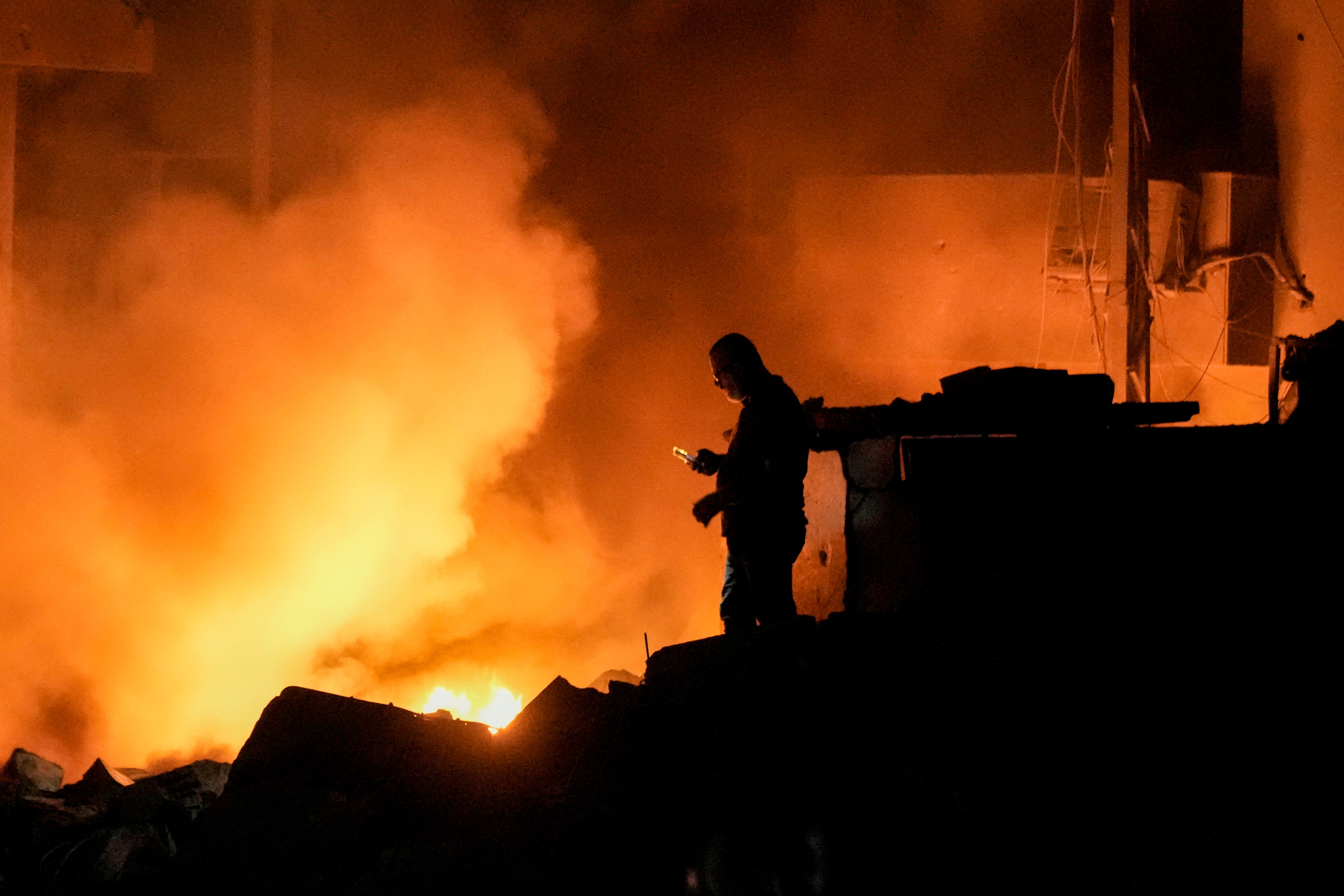 A man uses his mobile phone as flames and smoke rise at the site of buildings hit by an Israeli strike in central Beirut, Lebanon on Thursday. Photo: AP