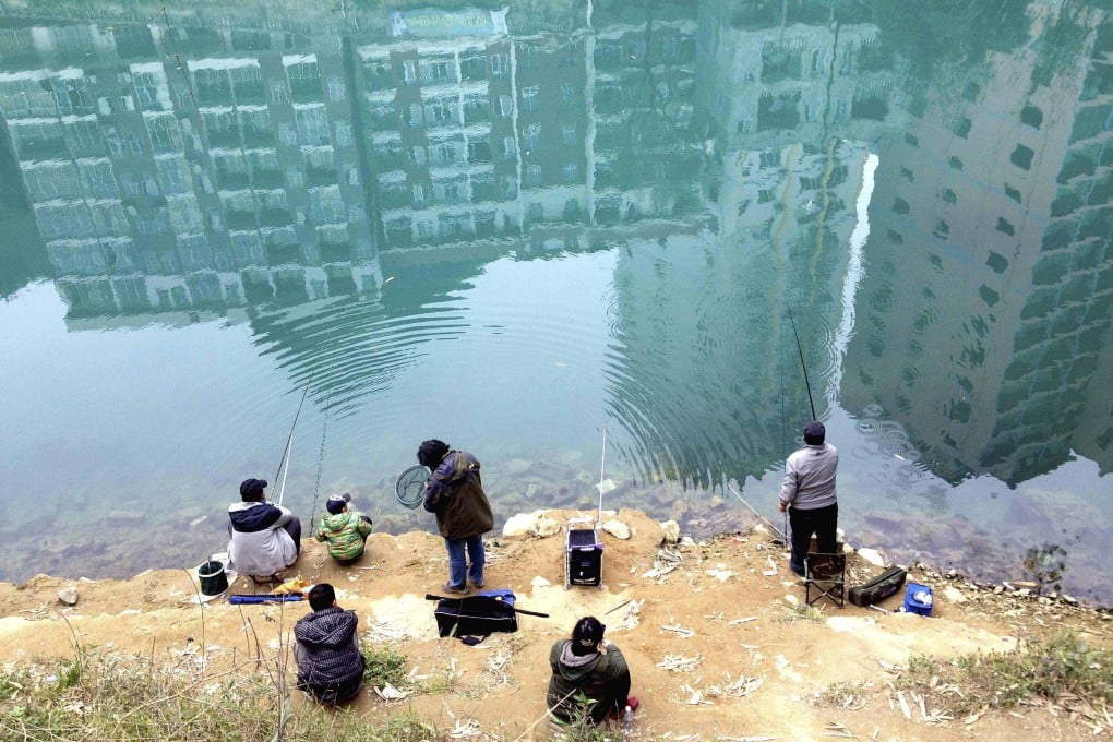 Residential buildings are reflected on the water as people fish in a river in Hechi in China’s Guangxi Zhuang autonomous region. Photo: Reuters